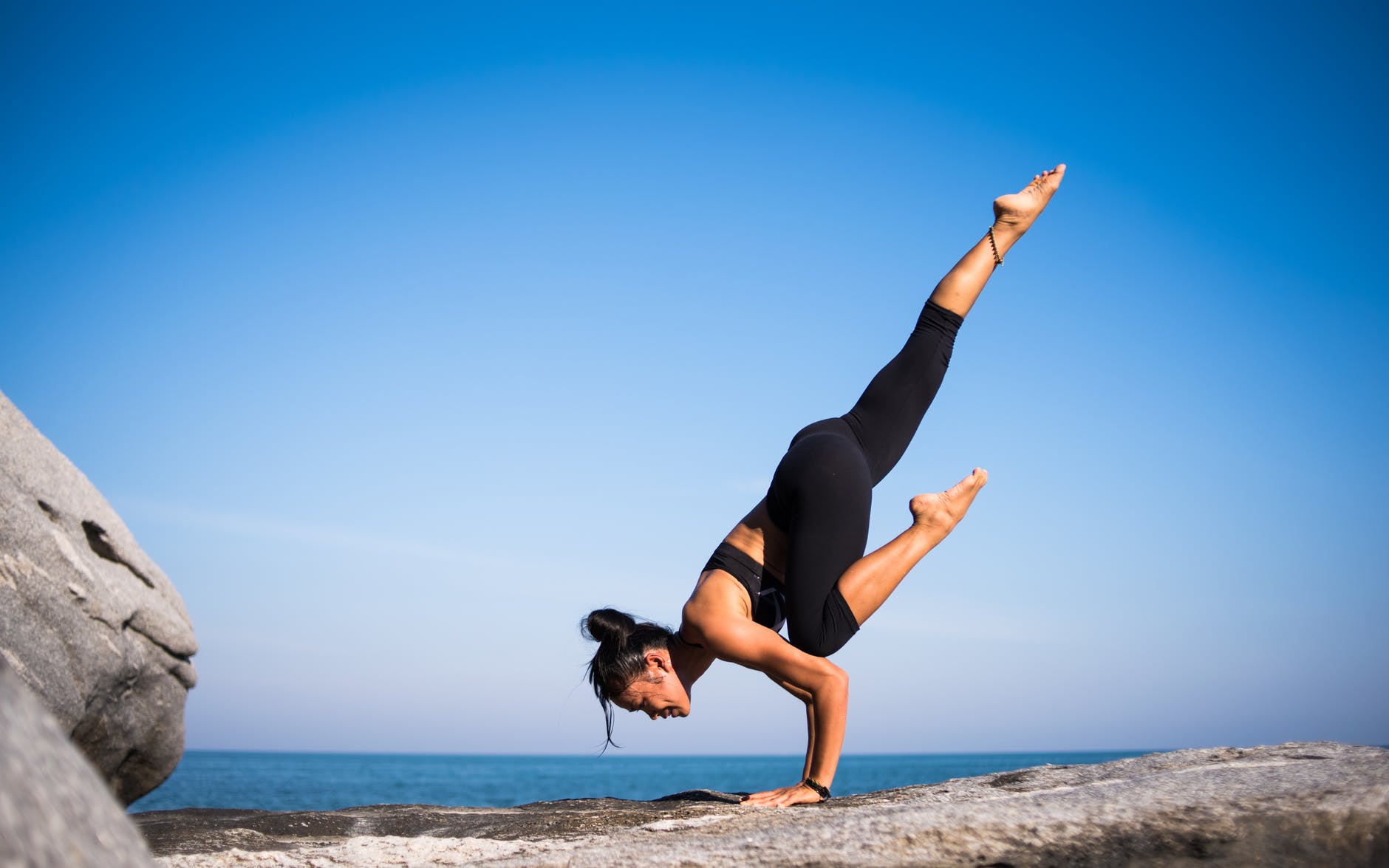 Woman doing yoga on a rock in front of the ocean