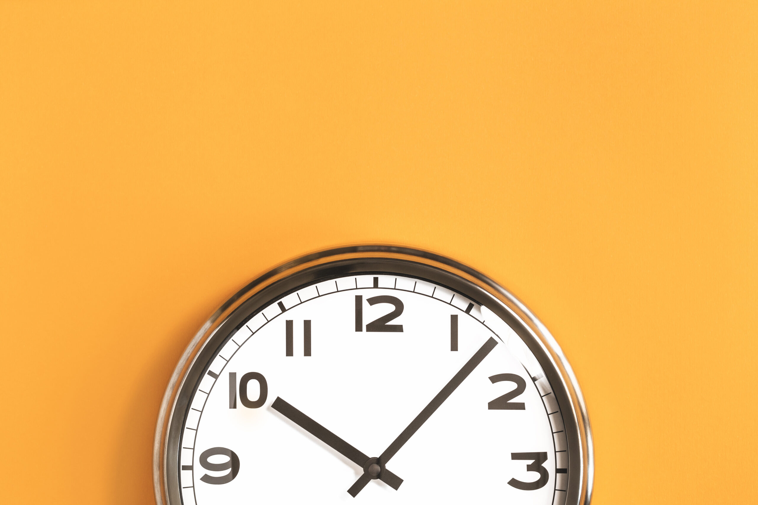 Part of analogue plain wall clock on trendy pastel orange background. Ten o'clock.
