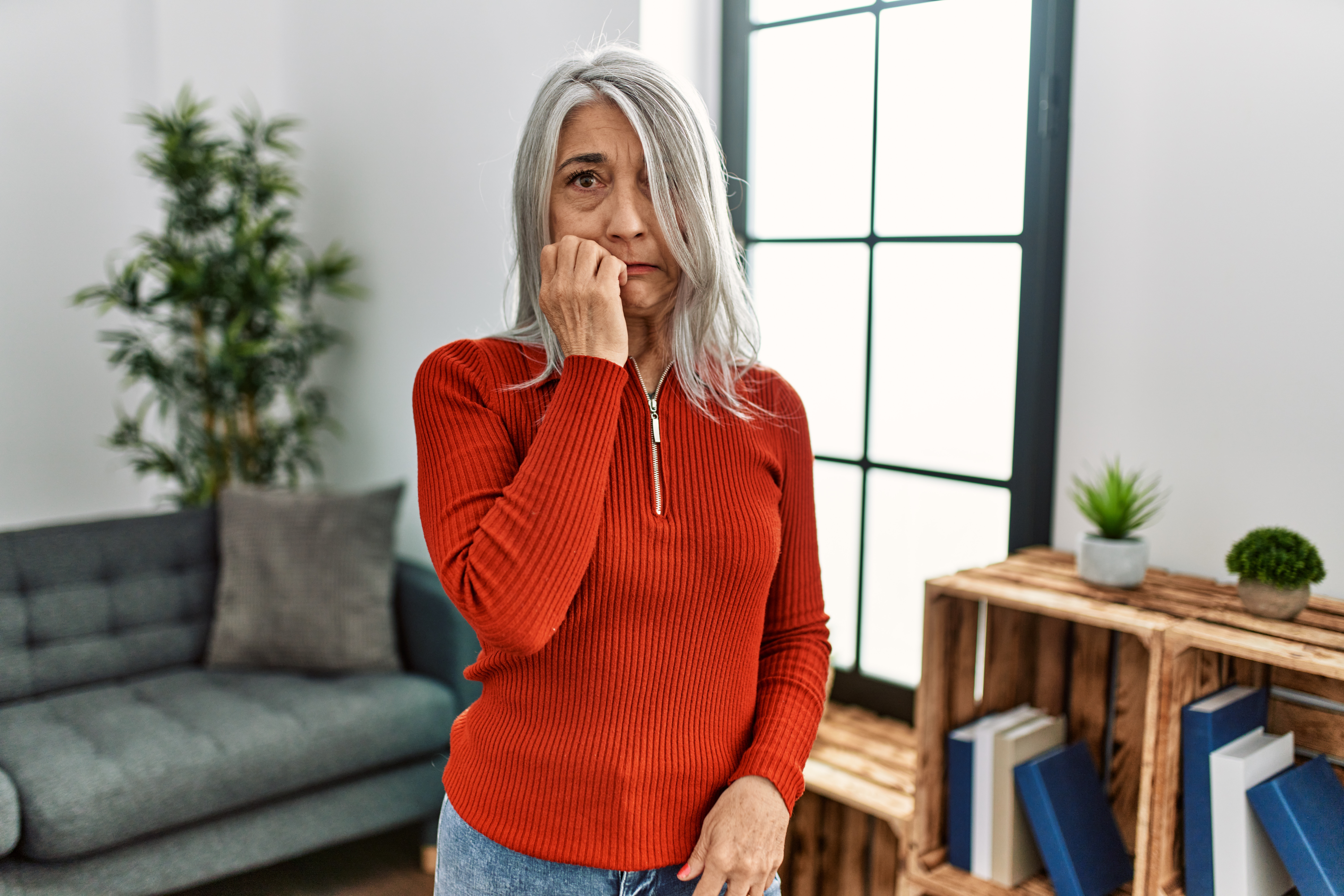 Middle age grey-haired woman wearing casual clothes standing at home looking stressed and nervous with hands on mouth biting nails. anxiety problem.