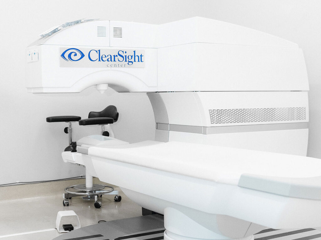 In a pristine clinical room, a white LASIK eye surgery machine labeled "ClearSight Center" stands next to a sleek black chair and stool.