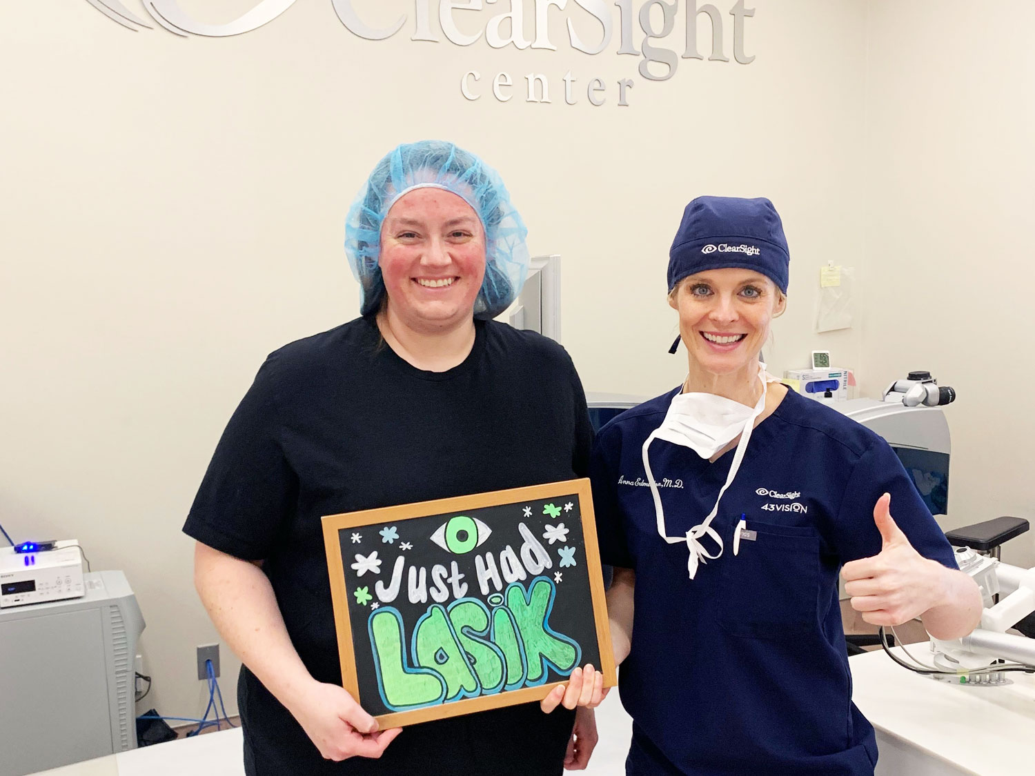 A person in scrubs smiles while another person holds a sign reading "Just Had LASIK eye surgery" at a ClearSight eye clinic.