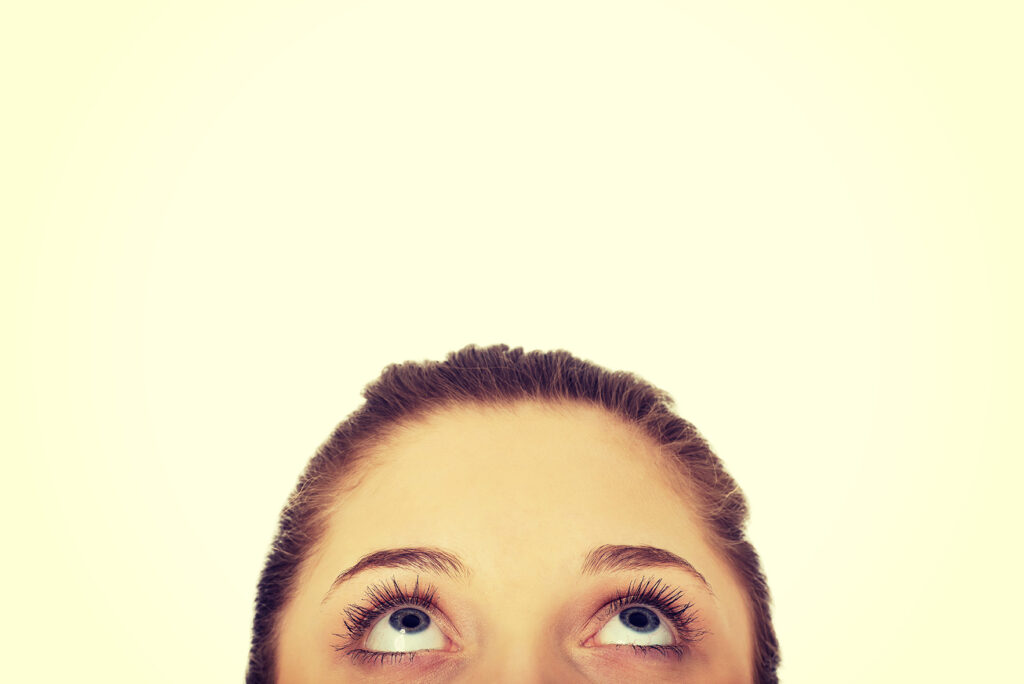 A person gazes upwards, contemplating the future benefits of ClearSight. With hair tied back, they leave a large blank space above, hinting at endless possibilities after LASIK eye surgery.