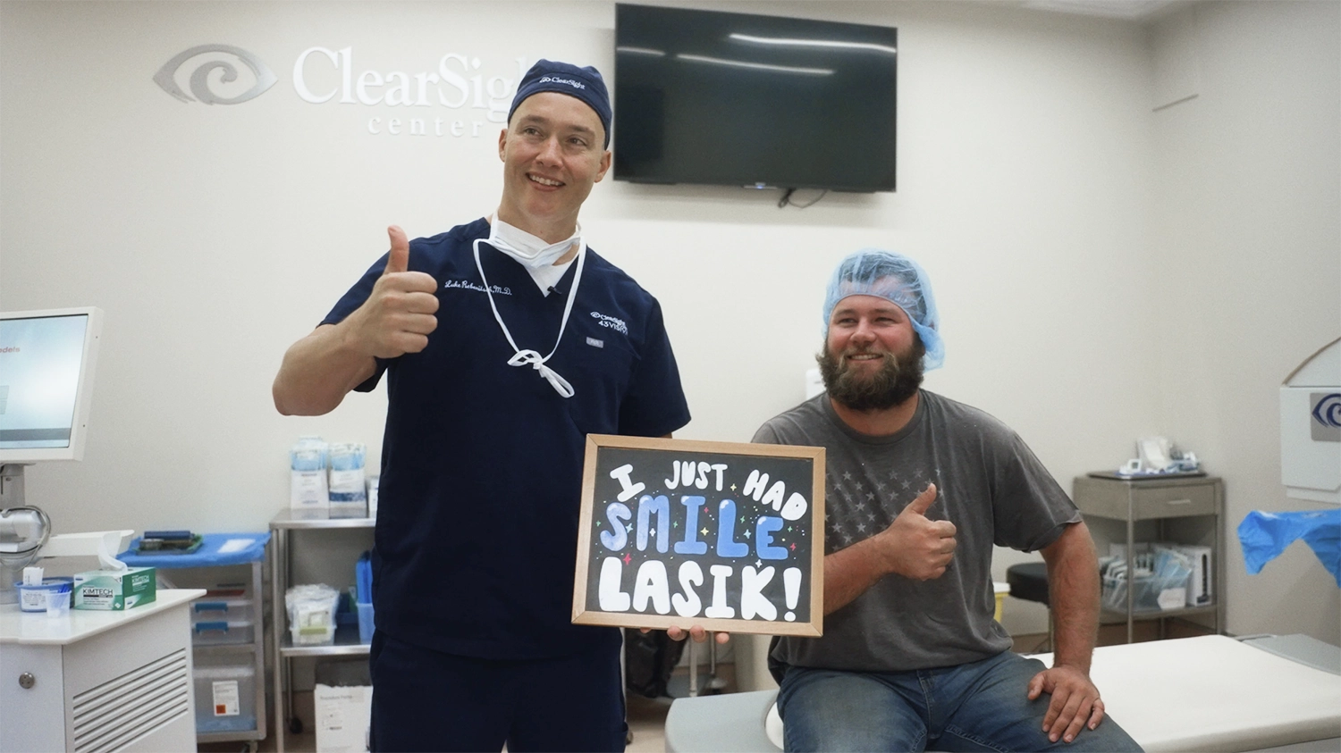 In a medical room, the doctor and patient both give thumbs up. The patient holds a sign reading, "I just had SMILE LASIK at ClearSight!.