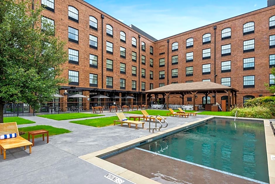 A brick building with multiple windows surrounds a courtyard where you will find a swimming pool, lounge chairs, greenery, and a covered seating area—a serene retreat that mirrors the clarity you might experience after Clearsight LASIK.