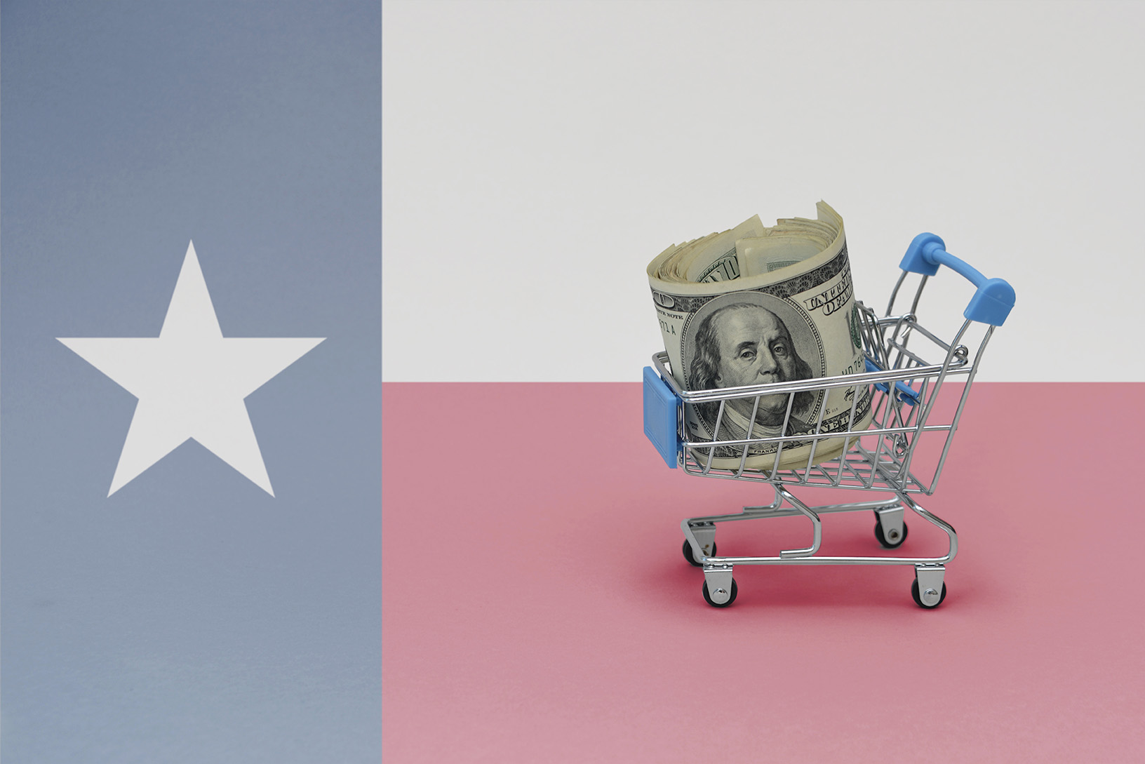 A roll of U.S. dollar bills sits in a mini shopping cart against a Texas flag background, symbolizing saving for future goals like LASIK eye surgery.